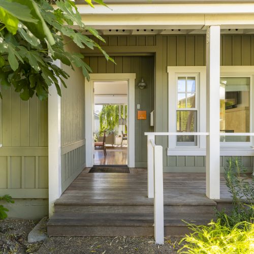 A bright home entryway with white columns, wooden porch steps, and lush green plants framing an open front door.