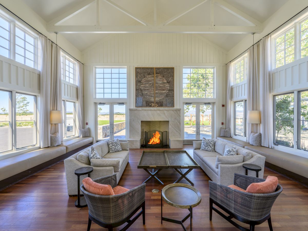 Bright modern living room with twin sofas, large windows, and a stone fireplace burning beneath two framed artworks.