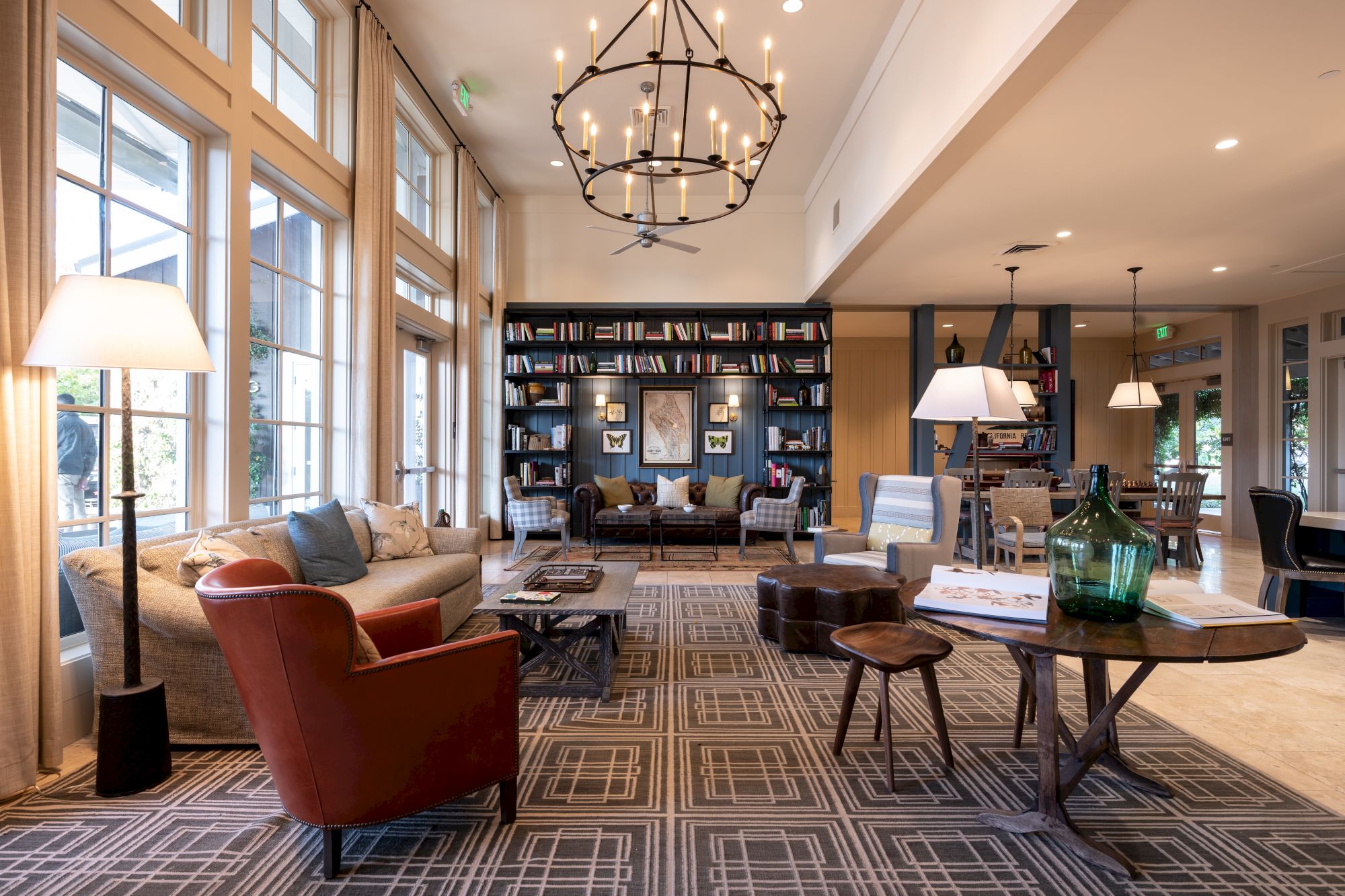 A bright lounge with sofas, bookshelves, lamps, rugs, and a large chandelier, plus chairs and coffee tables.